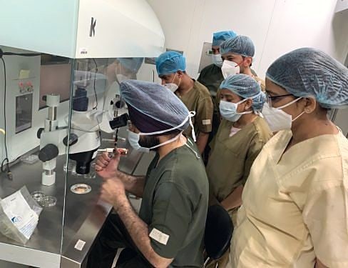 Trainees in scrubs gather around a lab bench with Dr. Sarabpreet Singh