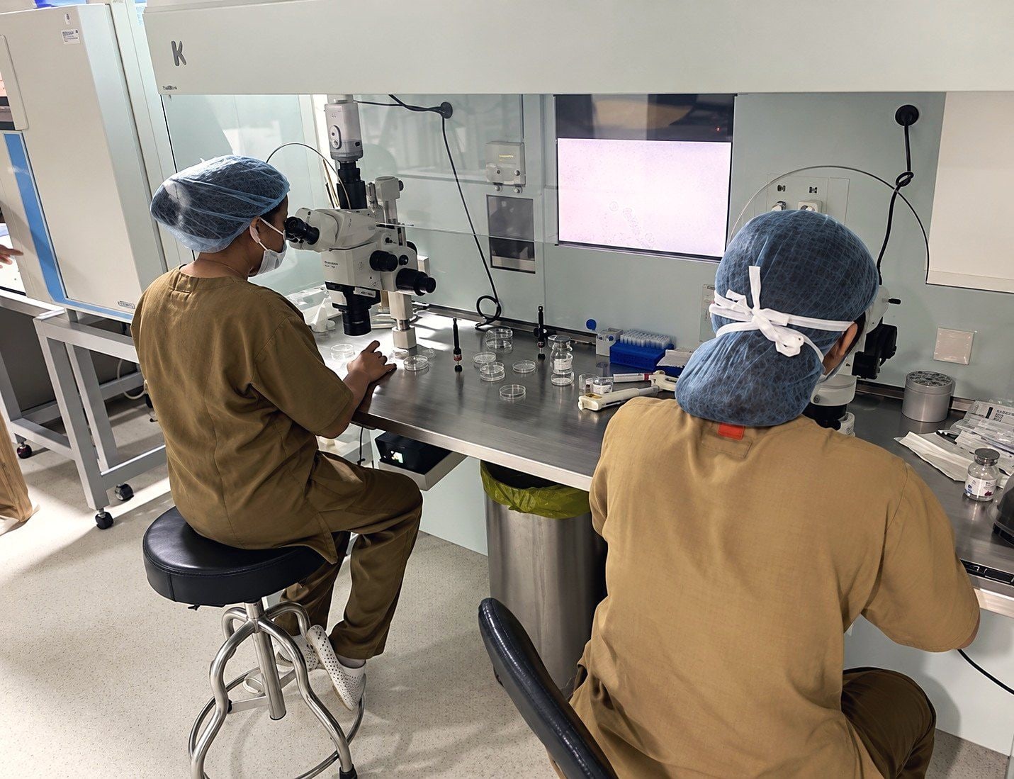 Two trainees work at microscope benches in the IVF lab