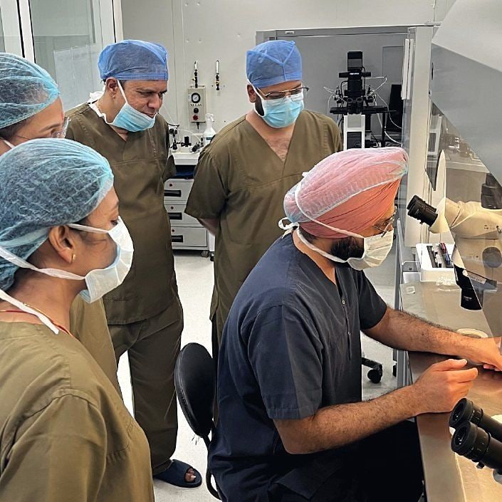 Dr. Sarabpreet Singh works at a microscope while trainees in scrubs watch