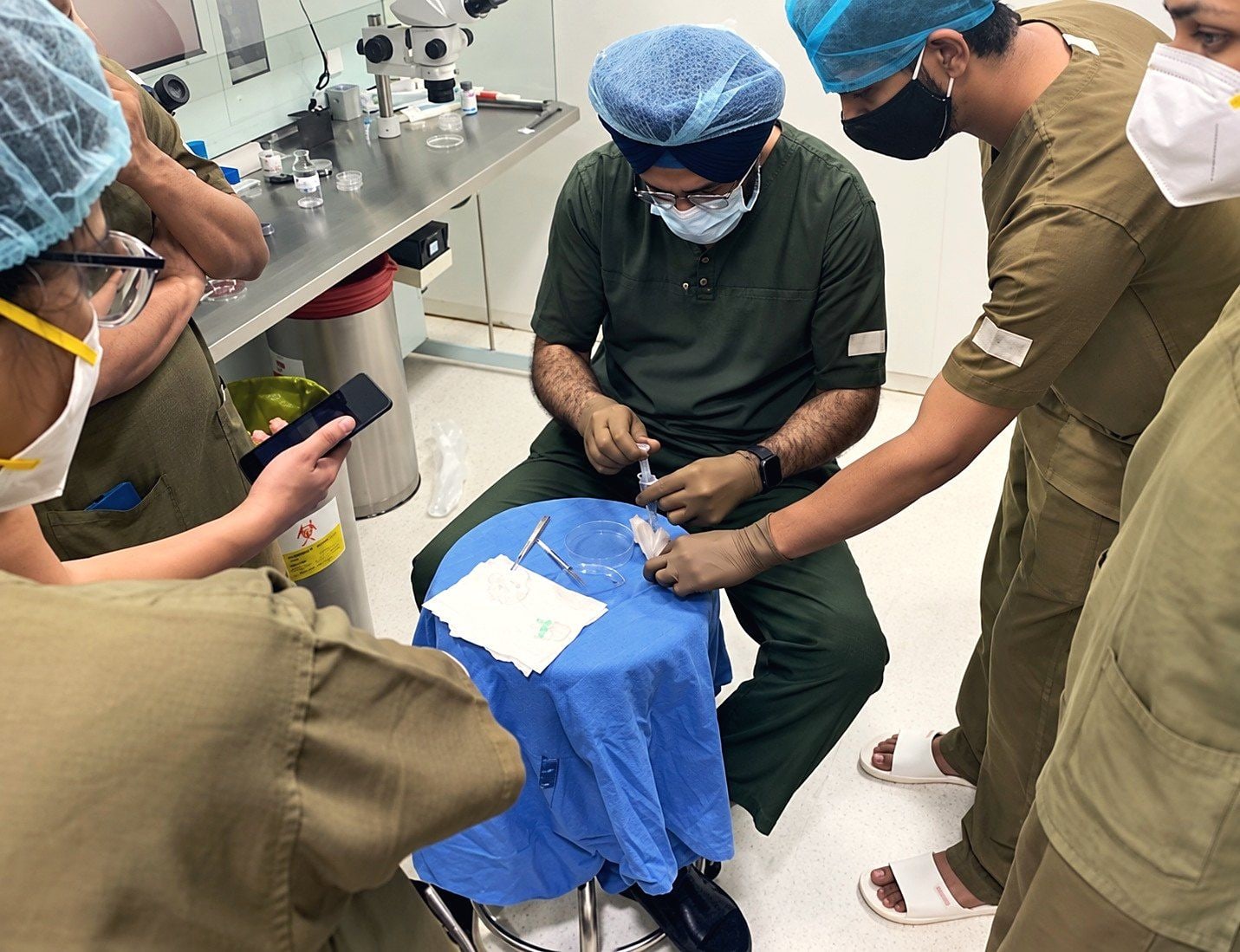 A faculty member demonstrates a procedure to trainees gathered around a draped stand